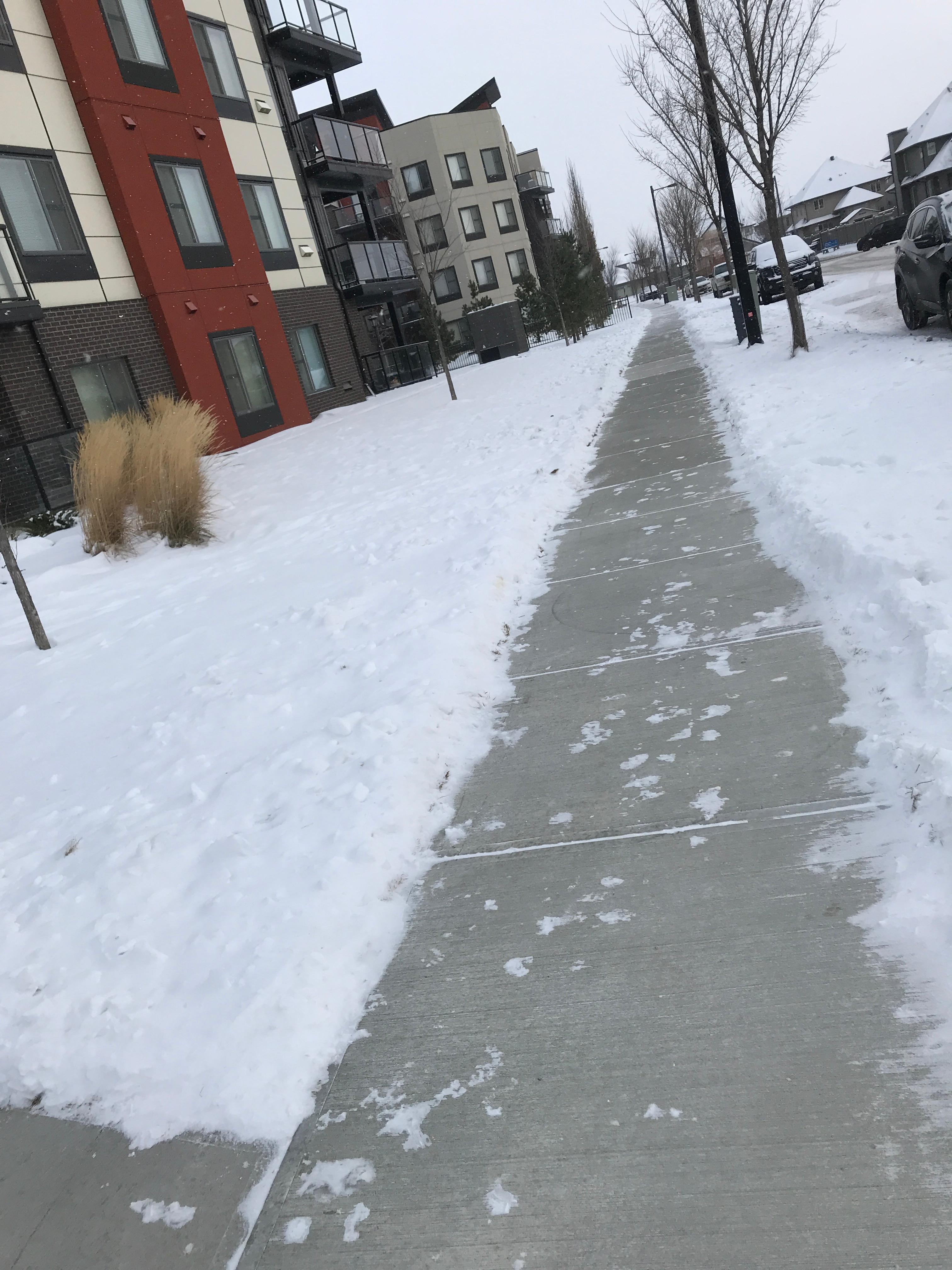 Long sidewalk beside apartment building cleared of snow